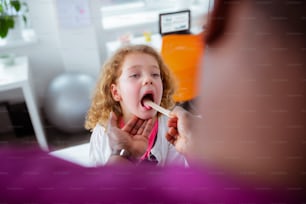 Bocca aperta. Riccio attraente bambina che apre la bocca per il pediatra mentre ha un forte mal di gola