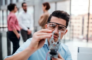 Ein junger Geschäftsmann oder Wissenschaftler mit Roboterhand und Schutzbrille steht im Büro und arbeitet.