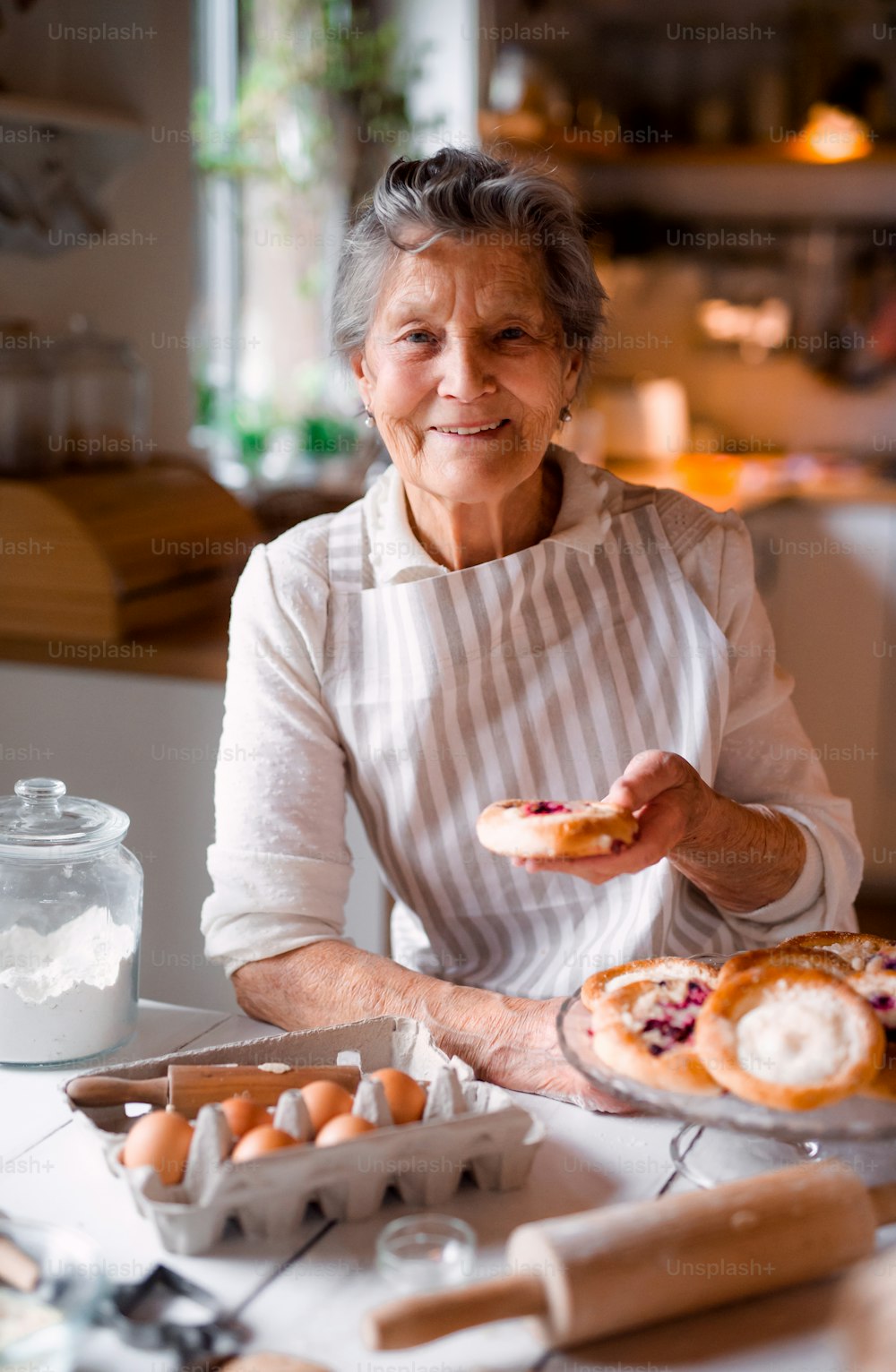 An elderly woman making cakes in a kitchen at home.