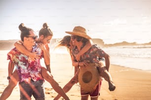 Cheerful people in sunny summer holiday vacation day - outdoor leisure activity with couples laughing a lot and have fun together in friendship - friends with golden sunet and ocean in background