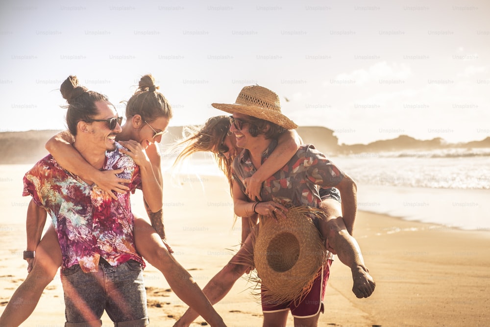 Cheerful people in sunny summer holiday vacation day - outdoor leisure activity with couples laughing a lot and have fun together in friendship - friends with golden sunet and ocean in background