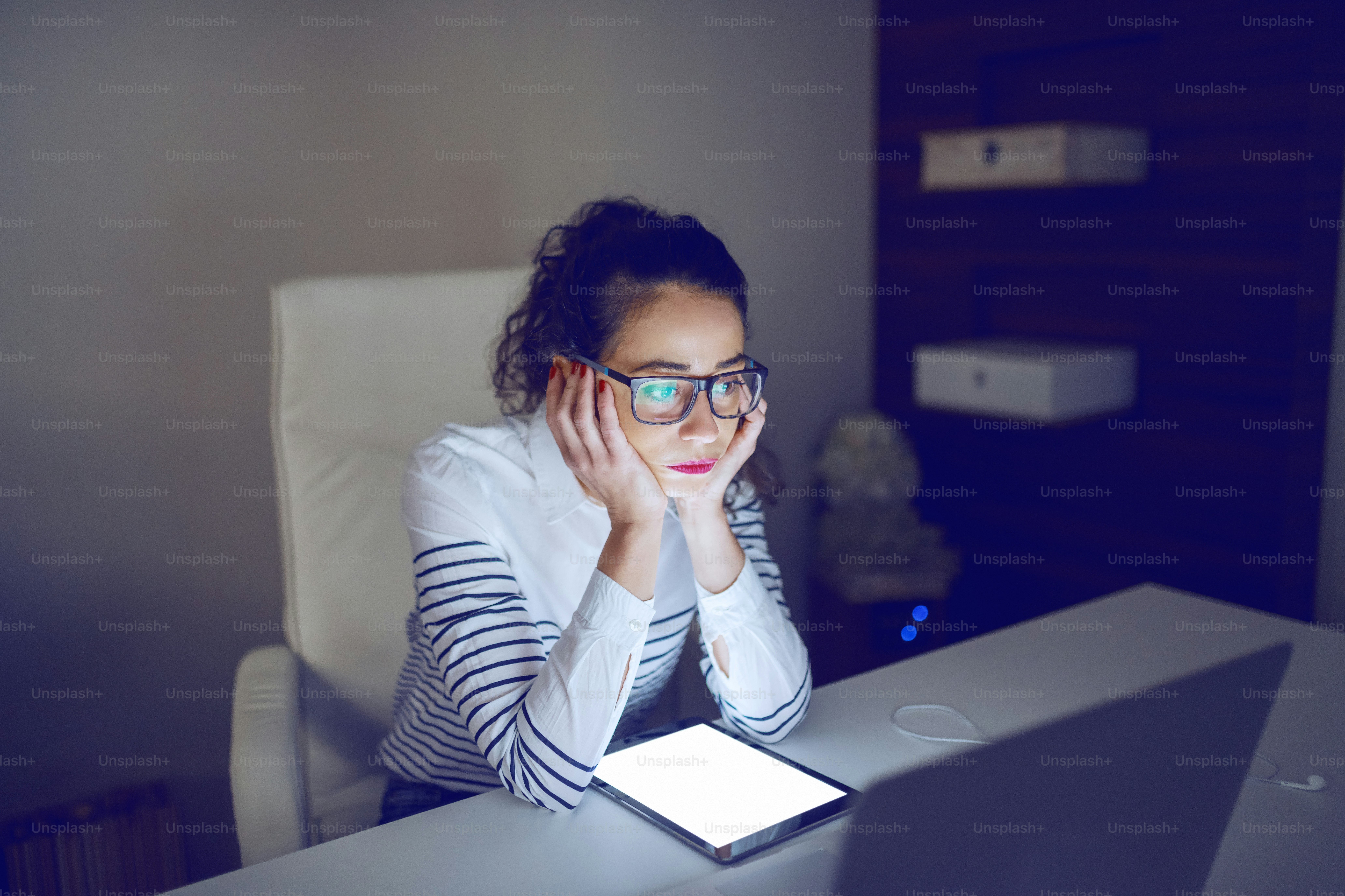 Portrait of depressed businesswoman sitting in office with head in hands and looking at laptop.