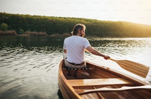 Rear view of male canoeist paddling the wooden canoe with oar.