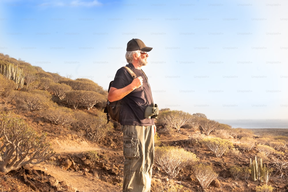 Happy senior man hiking an arid volcanic mountain. One caucasian people enjoying freedom and adventure. Looking at the horizon over water