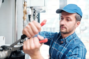 Jeune mécanicien contemporain du service d’entretien ménager réparant le tuyau dans la cuisine du client