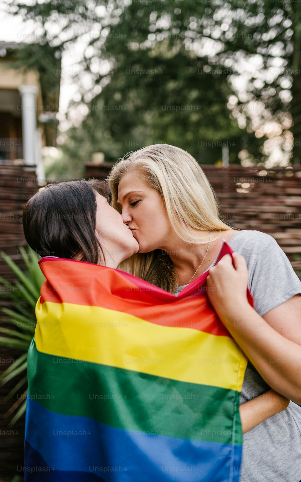 LGBT proud lesbian couple kissing holding gay rainbow flag