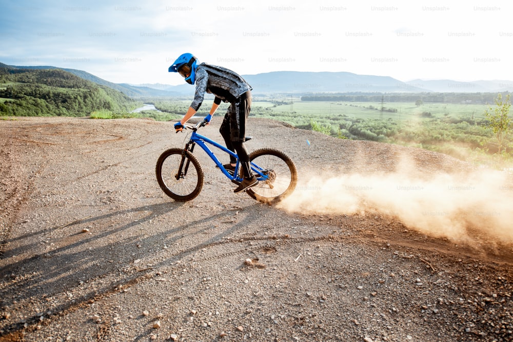 Ciclista profissional bem equipado andando extremamente nas montanhas rochosas levantando poeira para trás durante o pôr do sol