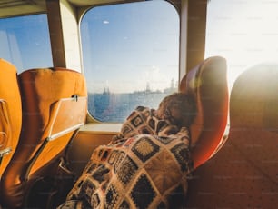 Mujer caucásica duerme durante el transporte del transbordador del crucero - concepción cansada para el estilo de vida del viaje y las vacaciones - sol a contraluz y océano fuera de la ventana