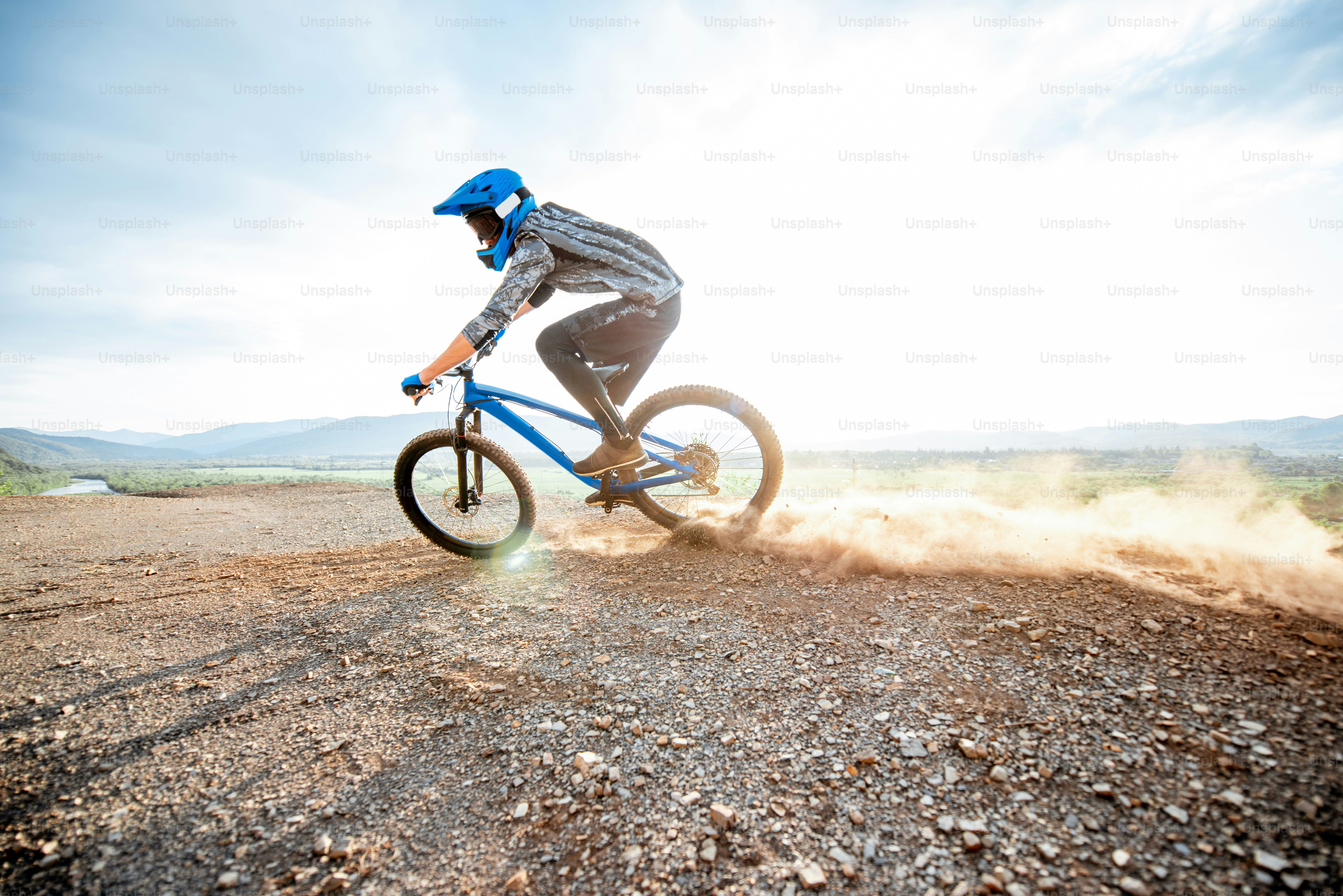 Professional well-equipped cyclist riding extremely on the rocky mountains raising dust behind during the sunset