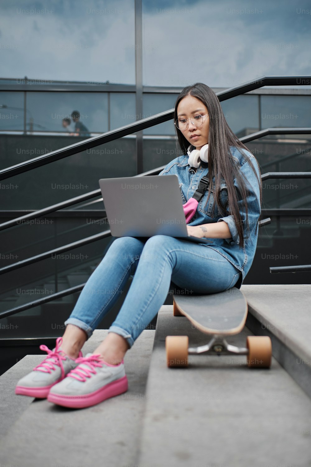 Full length photo of young freelancer skater girl sitting outside on longboard, working on laptop