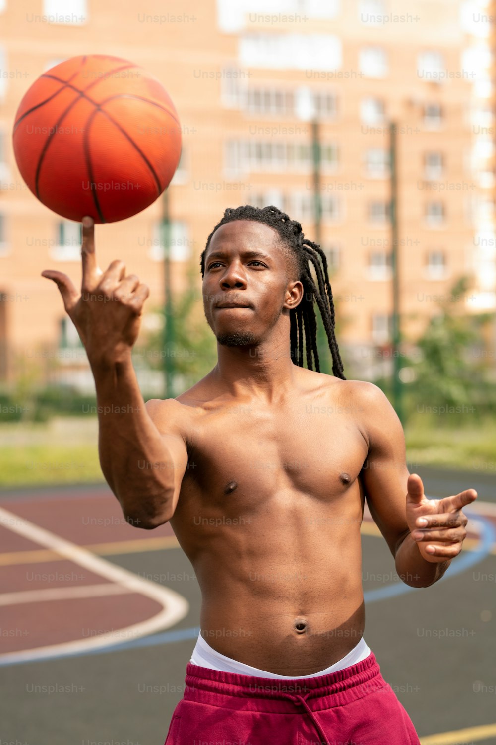 Junger afrikanischer Basketballspieler ohne Shirt, der den Ball auf dem Zeigefinger hält, während er ihn anschaut