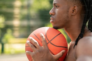 Side view of young multicultural shirtless sportsman holding ball between his chest and chin