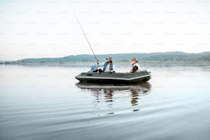 성인 아들과 함께 할아버지는 아침 일찍 잔잔한 물로 호수의 풍선 보트에서 낚시를 하고 있습니다. 넓은 풍경보기