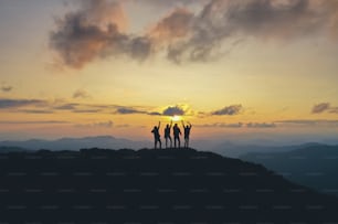 Les quatre personnes debout sur la belle montagne sur le fond du coucher du soleil