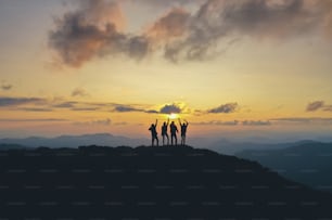 The four people standing on the beautiful mountain on the sunset background