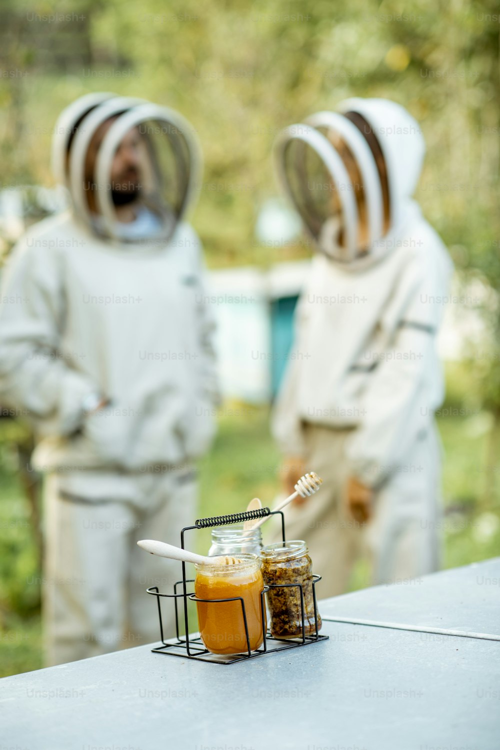 Jars with fresh honey and beeswax standing on the beehive with apiarists on the background