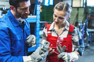 Mulher e homem trabalhadores satisfeitos verificando as medidas da peça de trabalho em metal