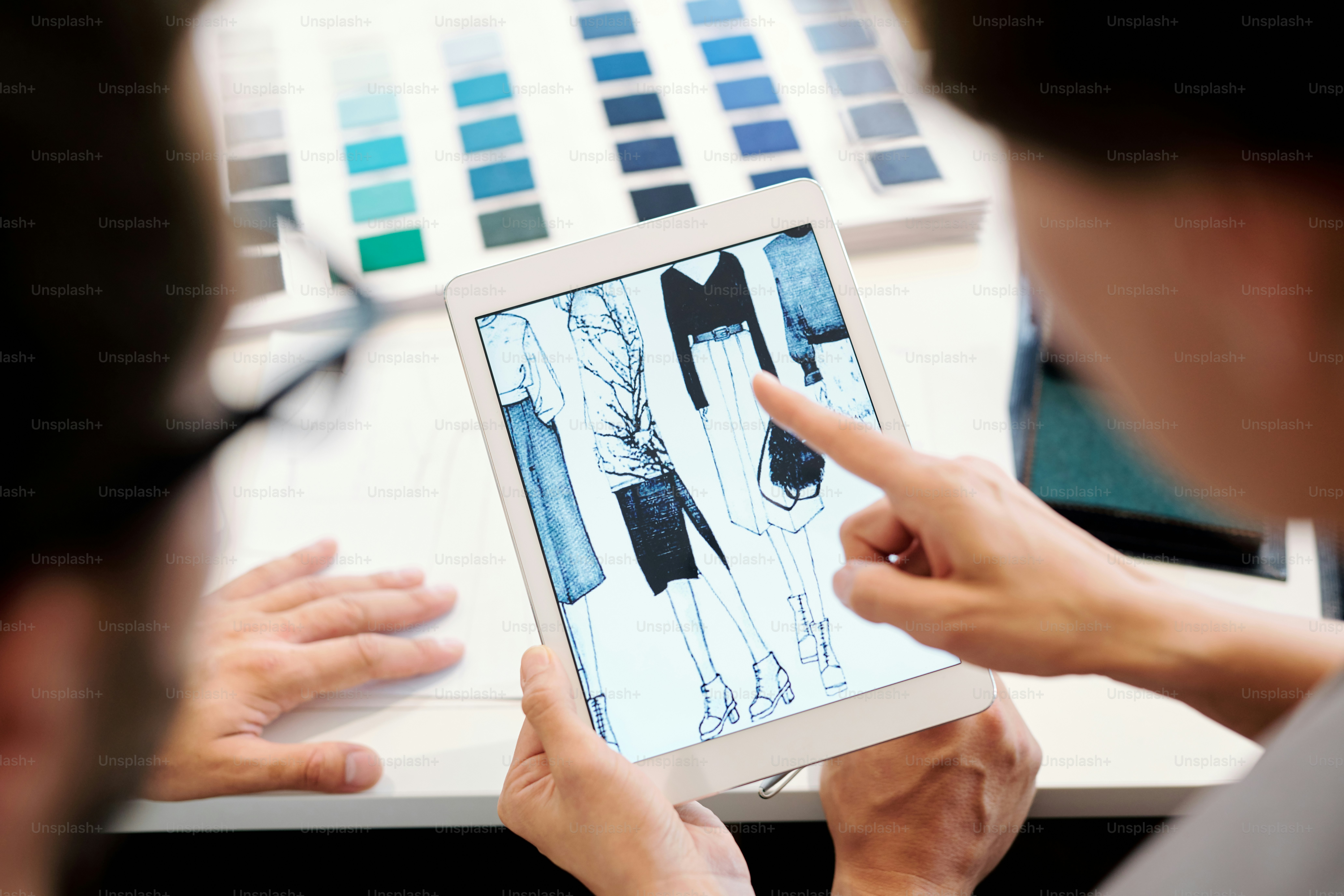 Uno de los jóvenes diseñadores de moda que señala la pantalla de la tableta mientras elige uno de los bocetos para su nueva colección