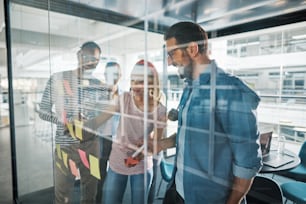 Smiling group of diverse businesspeople brainstorming with sticky notes on the glass wall of a modern boardroom in an office
