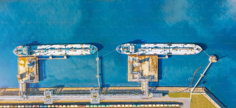 桟橋に液体燃料を積んだオイルターミナルと係留された2隻のタンカー、積み下ろし用の鉄道タンク車の空中上面図の広いパノラマ