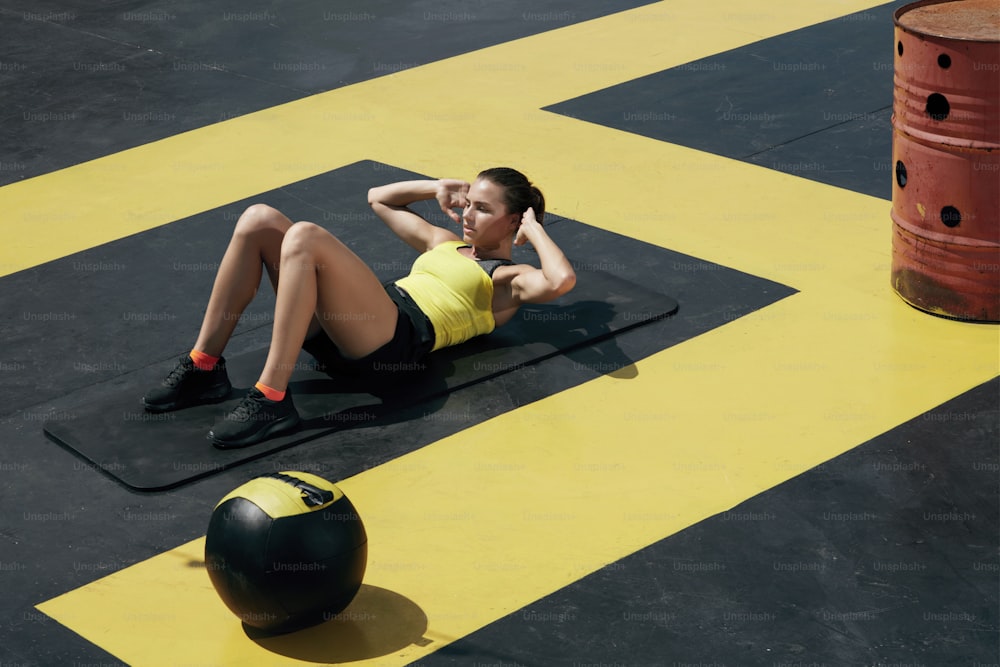 Mujer fitness haciendo abdominales en el gimnasio. Chica del deporte haciendo ejercicio en la estera de yoga, haciendo ejercicios de abdominales al aire libre en la calle