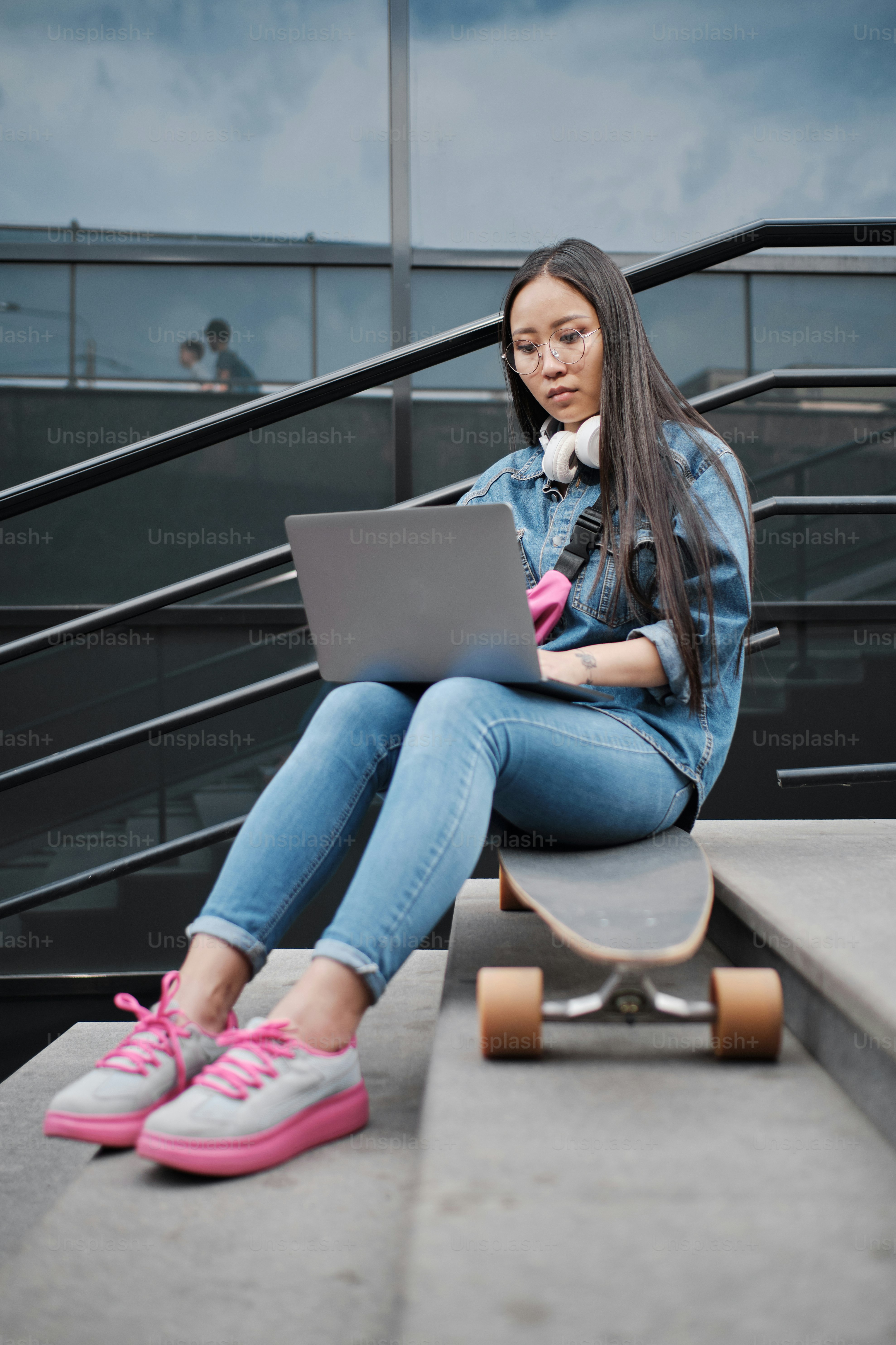 Foto in voller Länge eines jungen freiberuflichen Skatermädchens, das draußen auf dem Longboard sitzt und am Laptop arbeitet