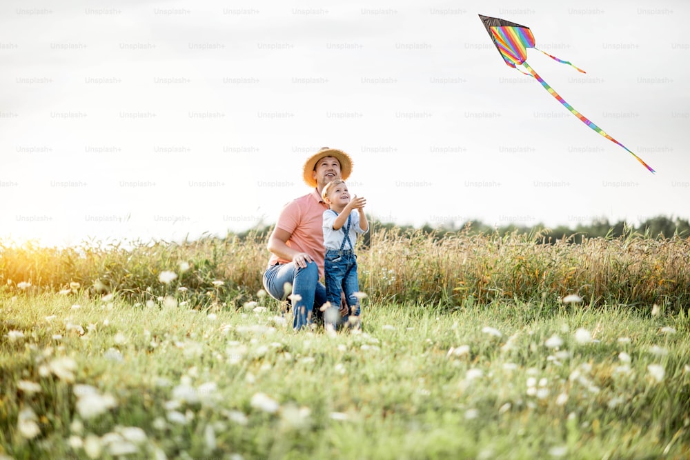 Pai com filho lançando pipa de ar colorida no campo durante o pôr do sol. Conceito de uma família feliz se divertindo durante a atividade de verão