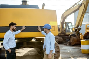 Constructor eligiendo maquinaria pesada para la construcción, hablando con un asesor de ventas en el campo abierto de una tienda con vehículos especiales