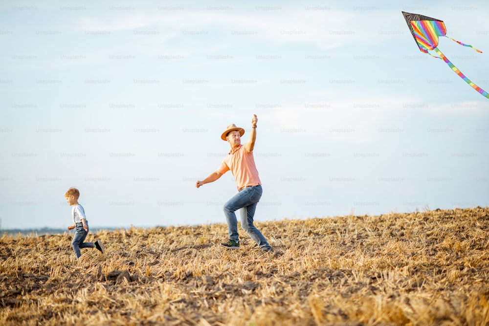 Padre con figlio che lancia un aquilone colorato sul campo. Concetto di una famiglia felice che si diverte durante l'attività estiva