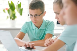 Two schoolboys concentrating on their schoolwork while sitting in front of laptop and looking through online information