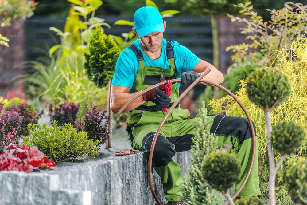 庭の灌漑散水システムを構築する40歳の白人男性。造園と庭の技術。