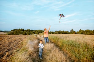 Padre con hijo lanzando cometa de aire colorida en el campo, amplia vista del paisaje con espacio de copia. Concepto de una familia feliz divirtiéndose durante la actividad de verano