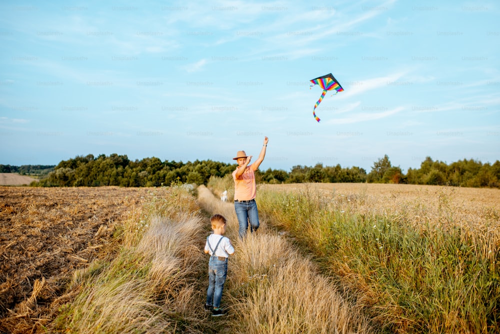 Pai com filho lançando pipa de ar colorida no campo, ampla vista da paisagem com espaço de cópia. Conceito de uma família feliz se divertindo durante a atividade de verão