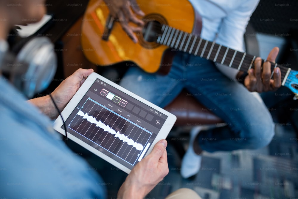 Digital tablet with sound waveforms on its display held by young contemporary musician during recording process