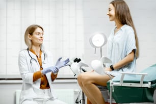 診察室の婦人科用椅子に座る妊婦の診察準備をする婦人科医