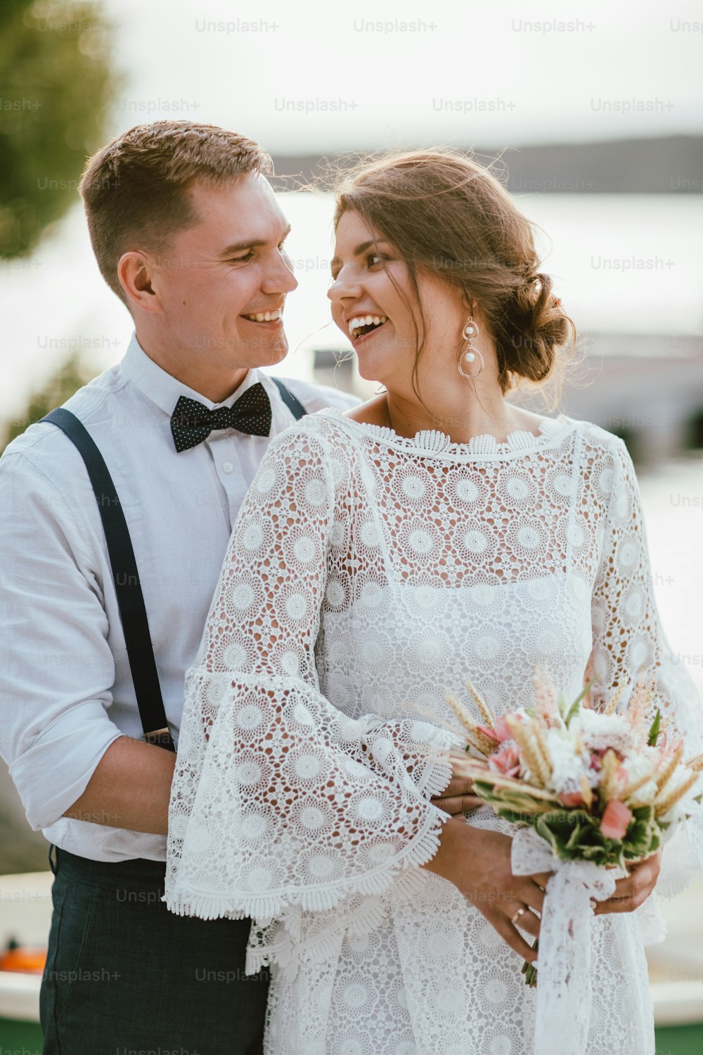 Happy newly married couple, smiling bride brunette young woman with the boho style bouquet with groom, close up portrait outdoors