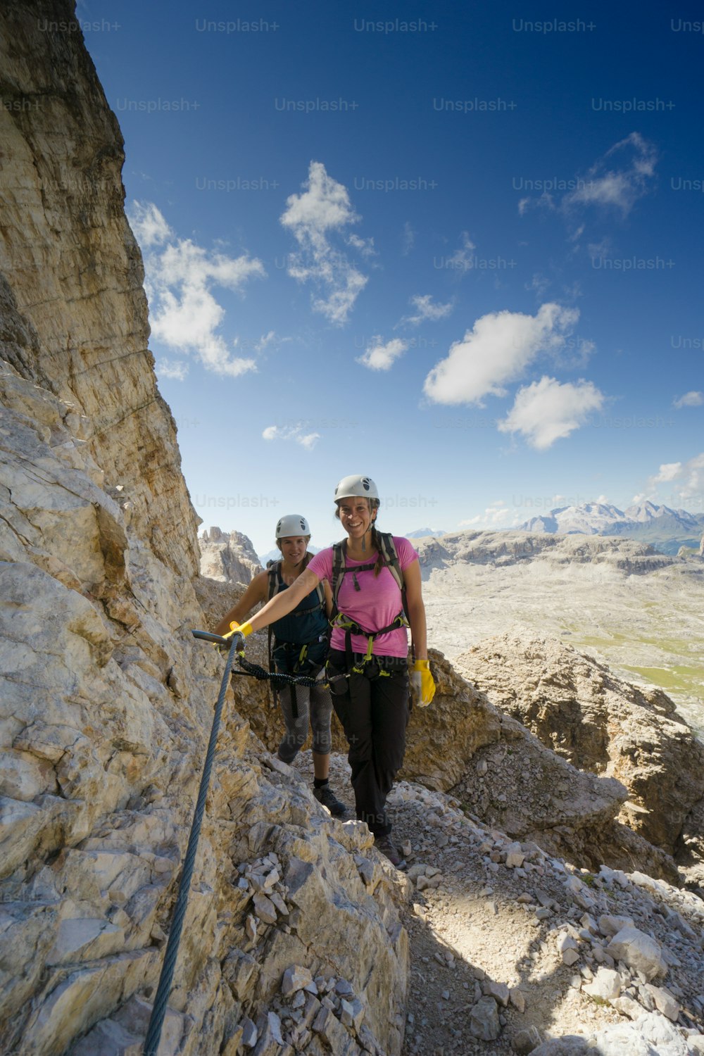 Vista vertical de una atractiva escaladora femenina y gemelas en una empinada vía ferrata en los Dolomitas italianos con una gran vista detrás