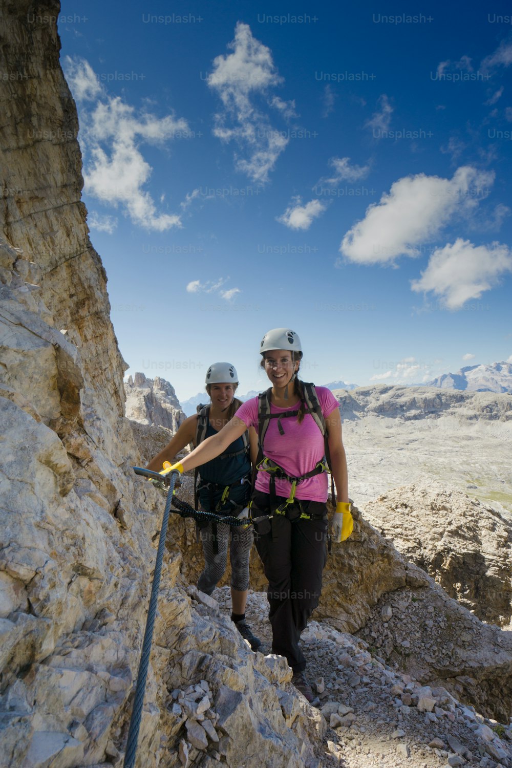 Vista verticale di un'attraente scalatrice e gemelle su una ripida via ferrata nelle Dolomiti italiane con una splendida vista alle spalle