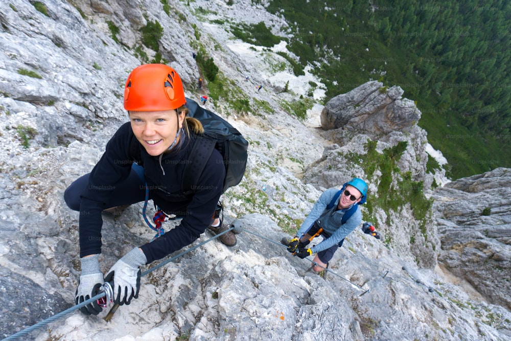 A man and woman in their twenties climb a steep Via Ferrata for fun during their holidays