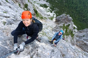 A man and woman in their twenties climb a steep Via Ferrata for fun during their holidays