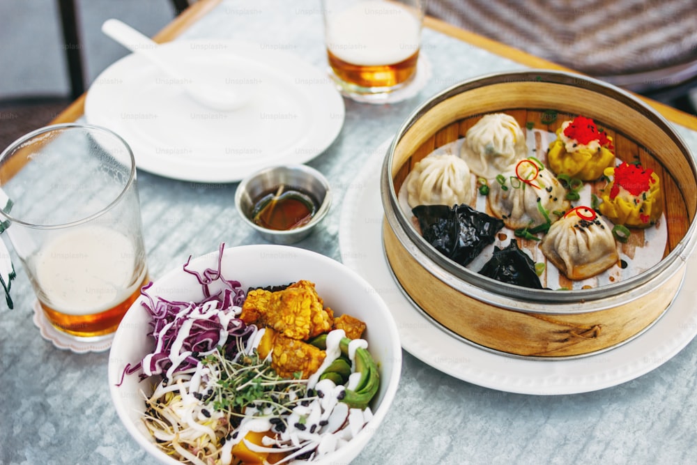 Panasiatisches Essen - verschiedene Dim Sums in einer Bambusschüssel und Salat. Mittagessen für zwei mit Bier
