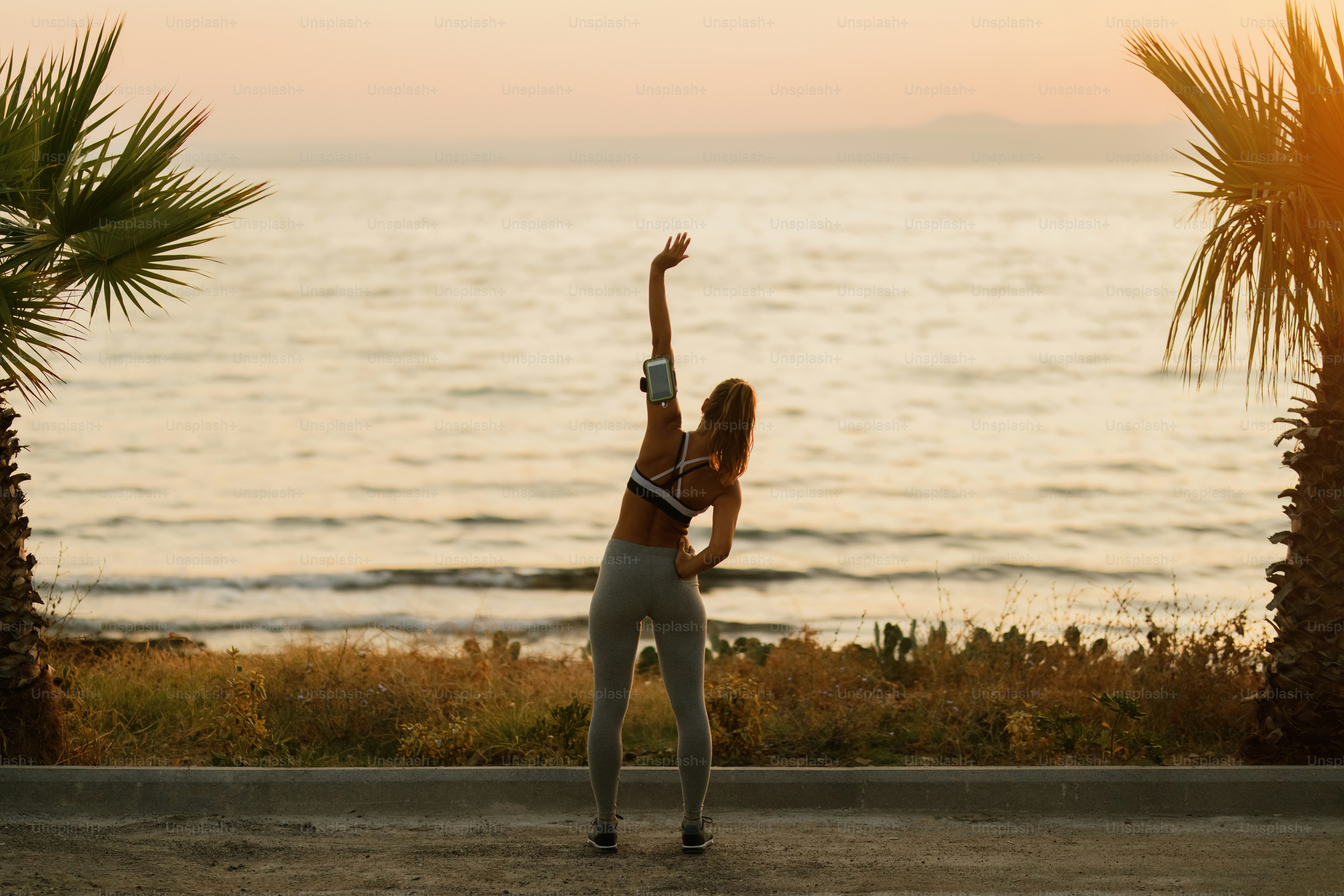 Rear view of athletic woman warming up before sports training by the sea at dawn. Copy space