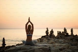 Rear view of Zen-lie woman practicing Yoga on a beach rock at sunset. Copy space.