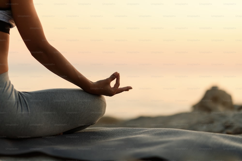 Close-up of woman practicing Yoga in lotus position at sunset. Copy space.
