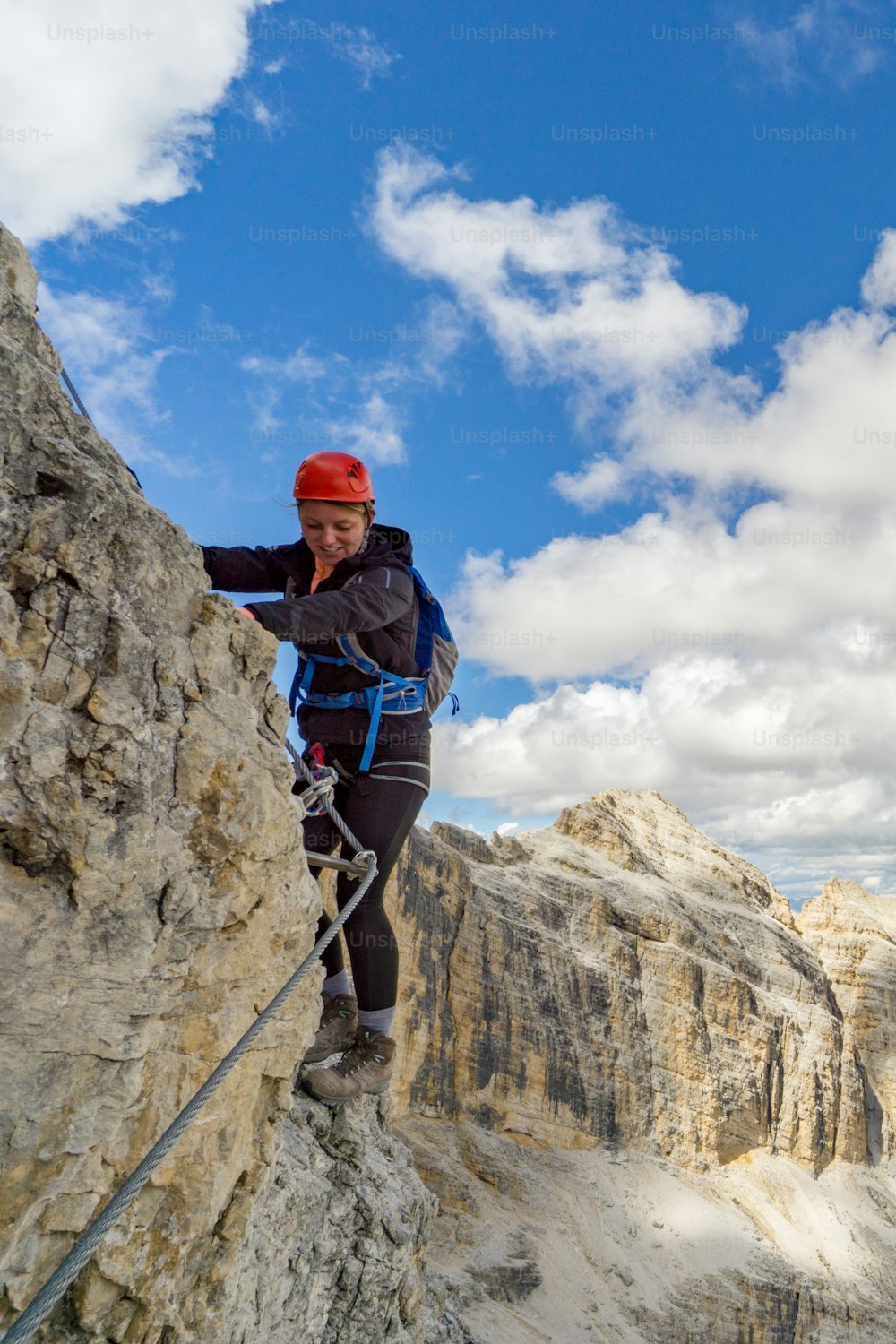 Vista verticale di un'attraente scalatrice bionda su una ripida via ferrata nelle Dolomiti italiane con una splendida vista alle spalle