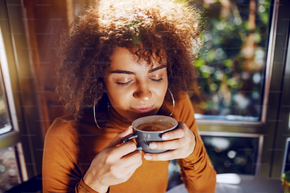 Retrato de una hermosa mujer joven de raza mixta con cabello rizado sentada en la cafetería y disfrutando del café.