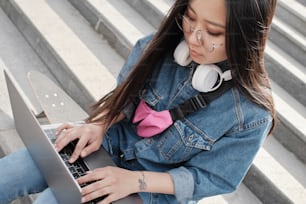 Close upyoung asian freelancer working on laptop while sitting on her longboard outdoors on stairs