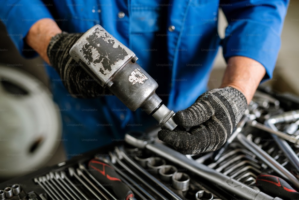 Gloved mechanic or repairman in workwear putting one of nozzles on metallic drill before carrying out repair work