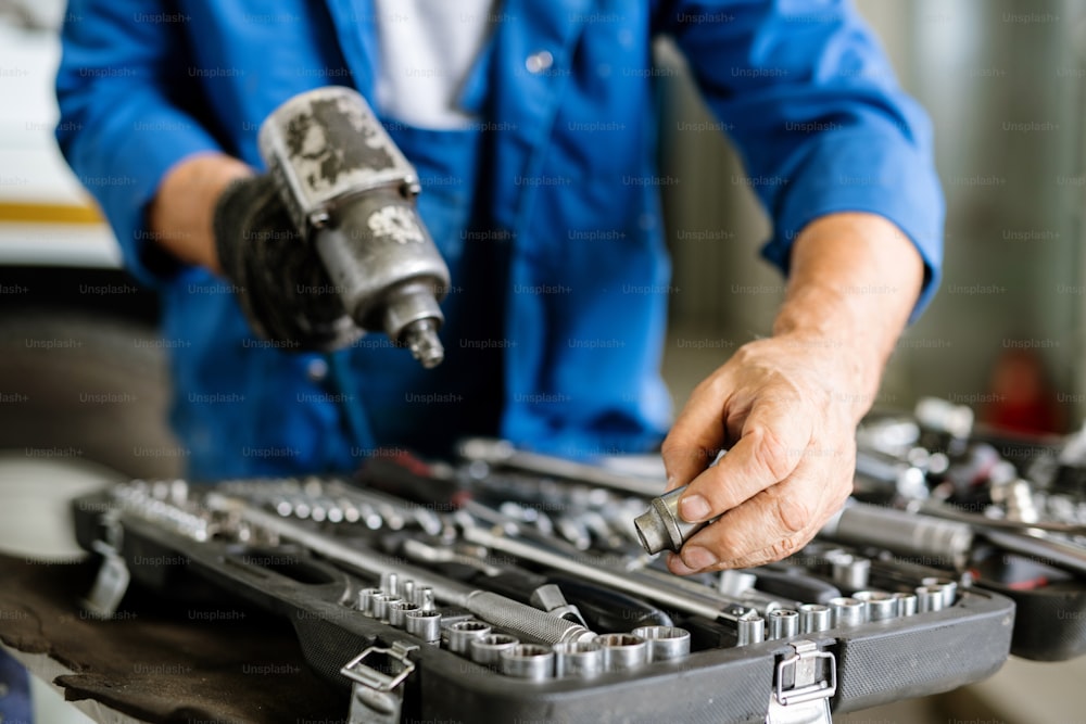 Mature technician or repairman taking one of iron nozzles for technical drill while standing by open kit of worktools