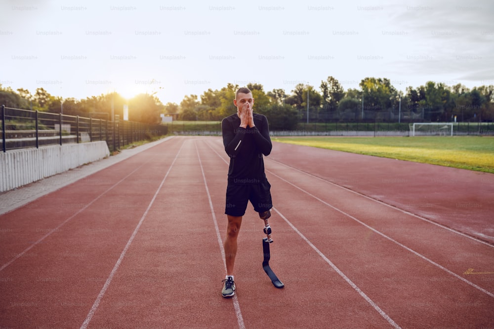 Uomo handicappato caucasico bello sportivo con gamba artificiale in piedi sulla pista e che si prepara a correre.